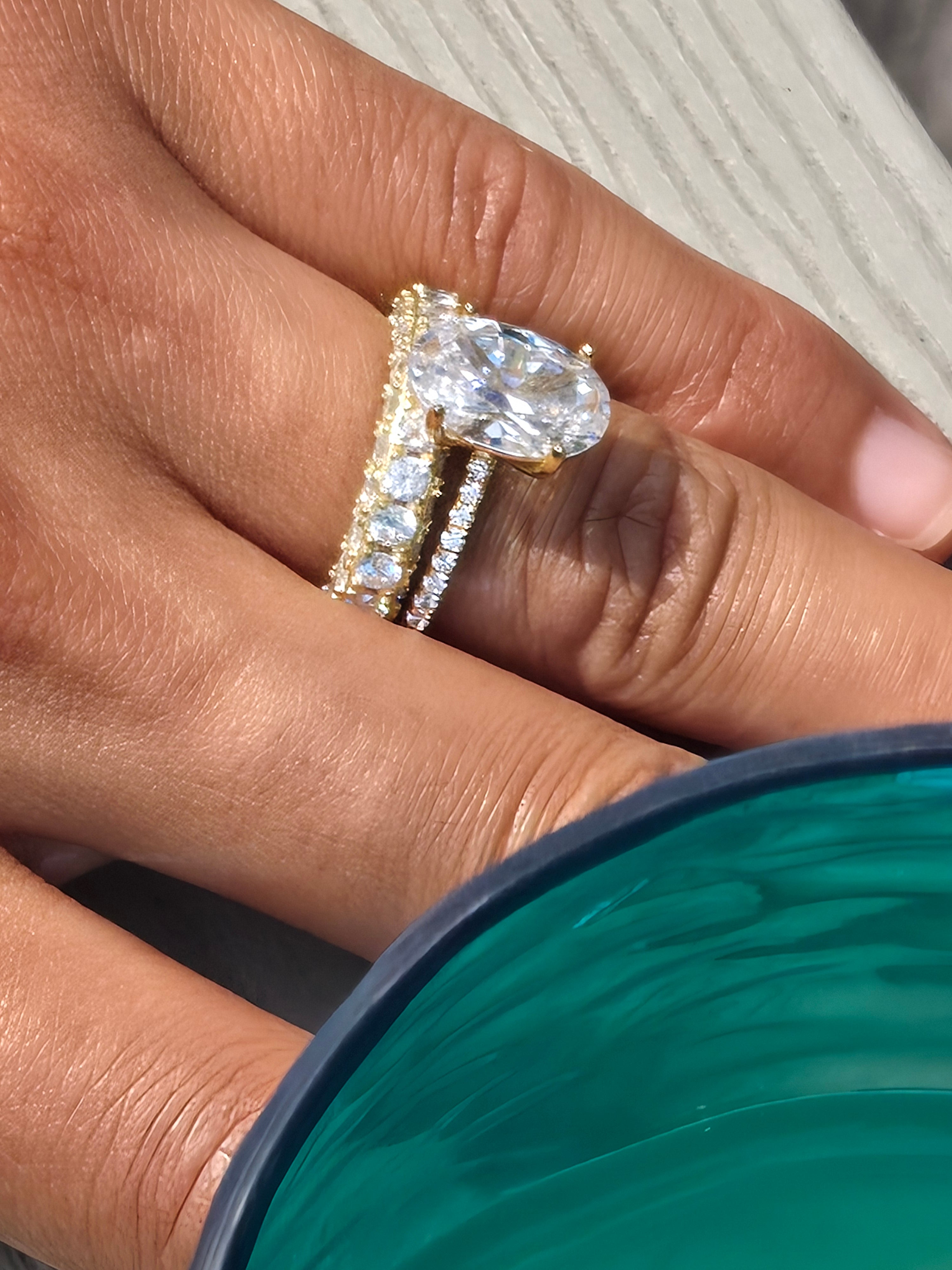Close-up of a hand wearing two diamond rings with a teal container in the background.