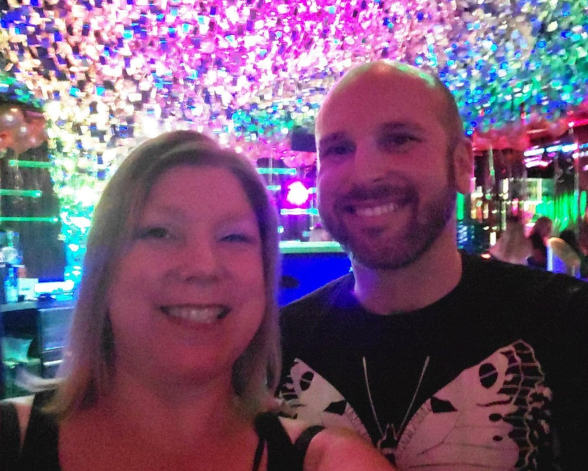 Two people posing for a selfie in front of a colorful, light-up wall.