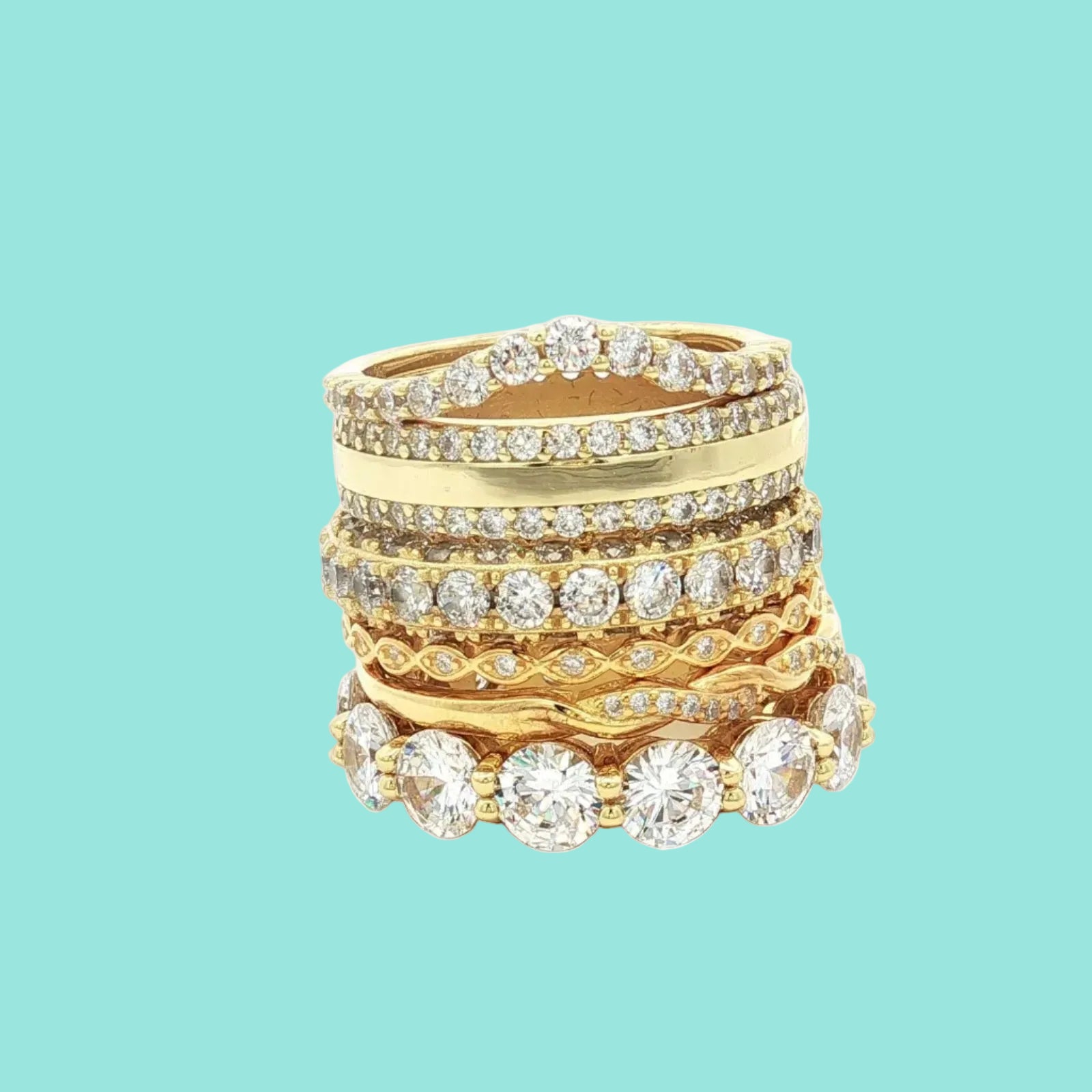 Stack of gold rings with brilliant white CZ stones on a light teal background 