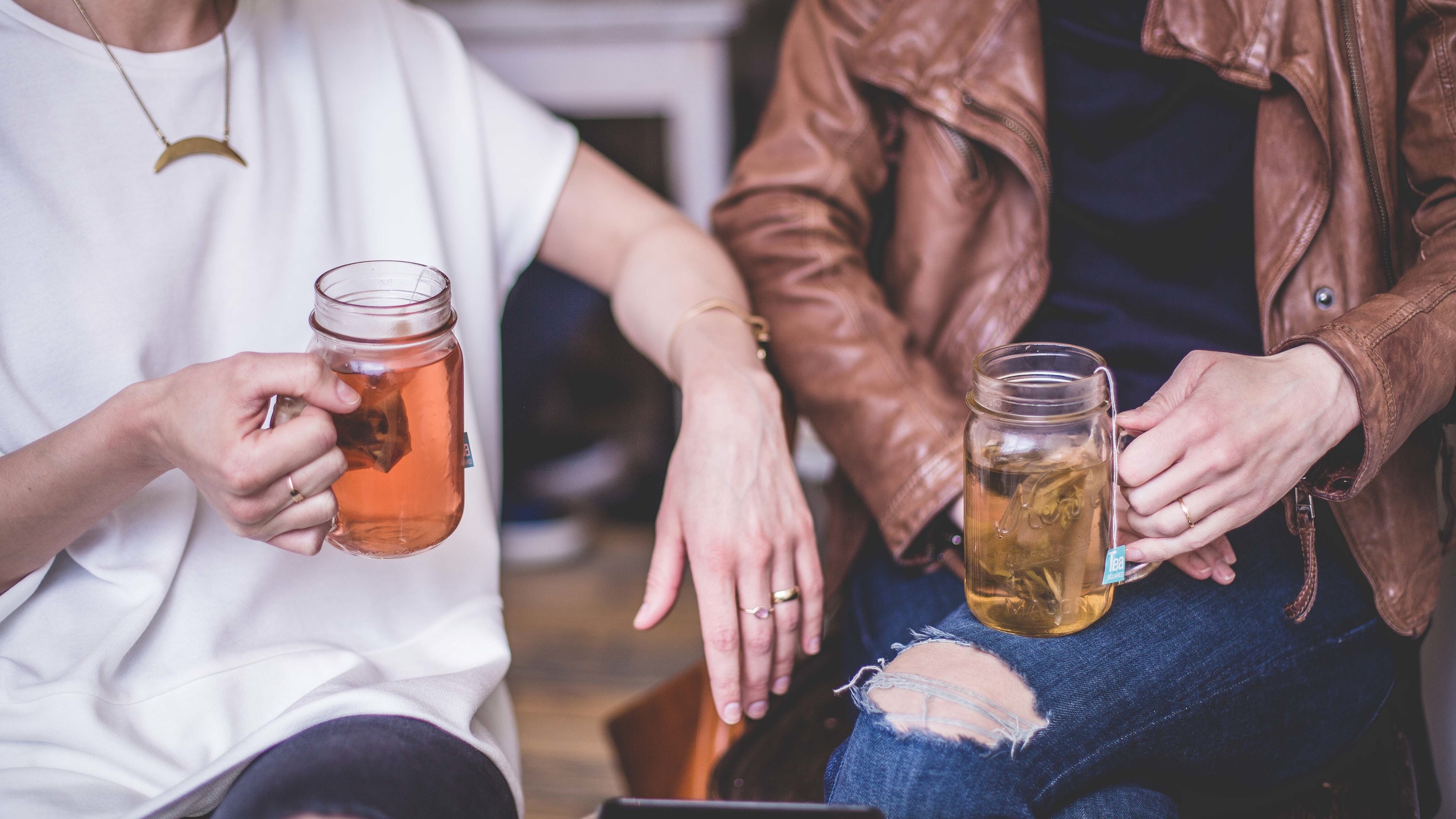 Two women wearing jewelry, relaxing in a lounge together and drinking tea.